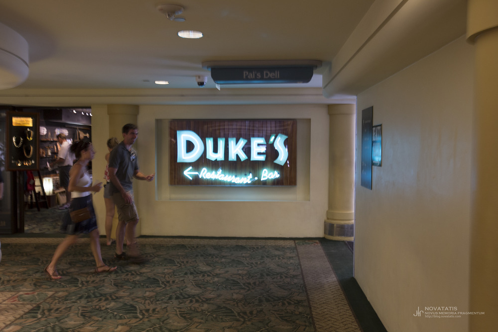 Duke’s 간판 앞을 지나는 복도 속 행인들