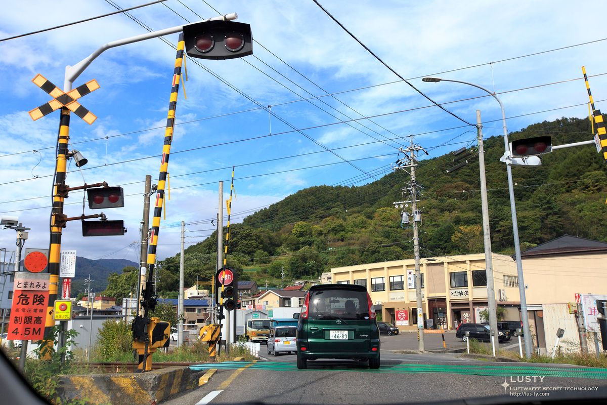 도로 위 철도 건널목 신호등과 초록 승용차