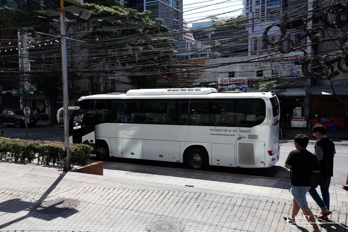 도로변 주차된 흰 투어 버스 옆 보행자들
